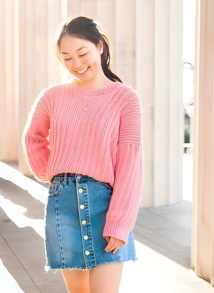 smiling woman wearing a pink crochet jumper and a denim skirt