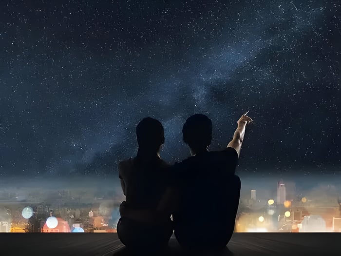 a couple pointing at a starry sky at night