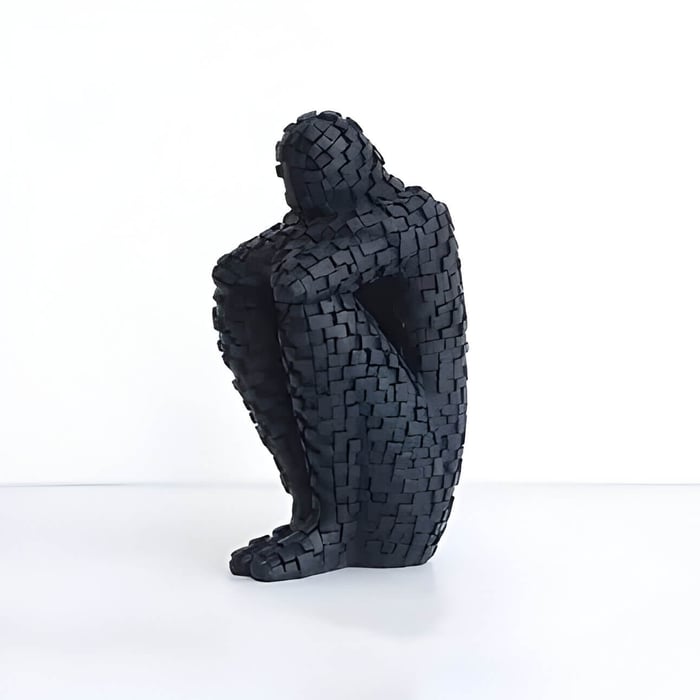 a black textured sculpture of a person sitting with their head resting on their legs