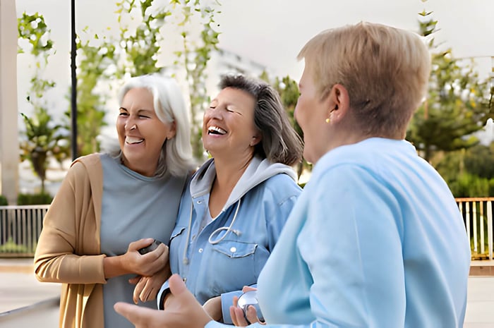 3 older ladies, linking arms, smiling and laughing outside