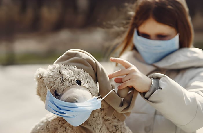 a young girl and her teddy bear wearing a face mask