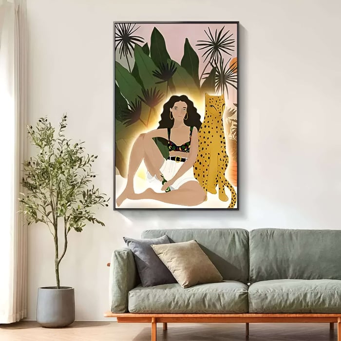 Framed modern illustration above a gray sofa showing a seated woman in white shorts beside a spotted cheetah, set against large tropical leaves with a warm halo glow.