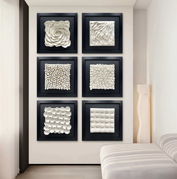 A minimalist room features six Harmonia 3D Spiral Wall Sculpture pieces from Giant Sculptures, arranged in two columns. Each has a unique textured pattern. A white modern chair sits nearby, with soft natural light filling the space, evoking ceramic wall sculptures.