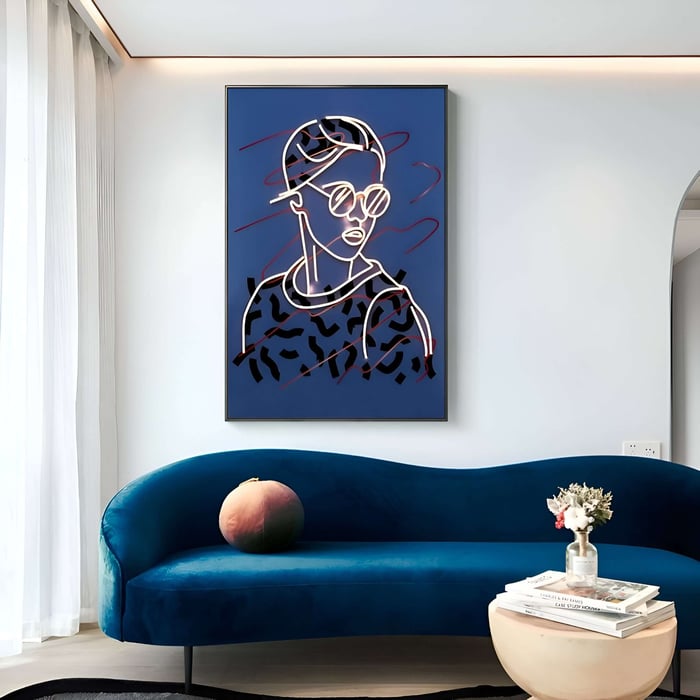 A modern living room with a blue velvet couch, a small round coffee table holding pink and white flowers, and Giant Sculptures Polaris Urban Vogue Crystal Porcelain LED 3D art featuring an abstract portrait of a person in sunglasses and a cap.
