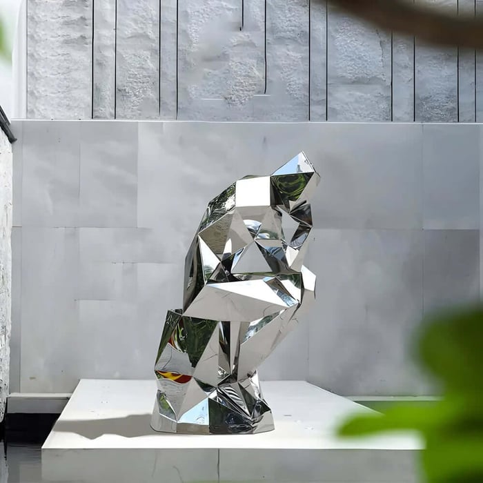 Mirror-finish faceted bear geometric sculpture on a white plinth against a stone wall.