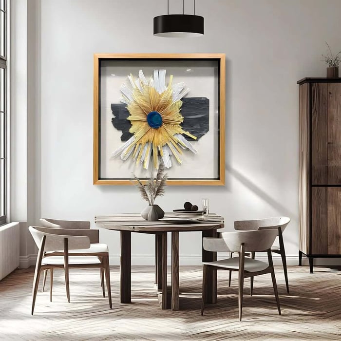Modern framed mixed media art with a gold sunburst design and blue centre above a dining table.