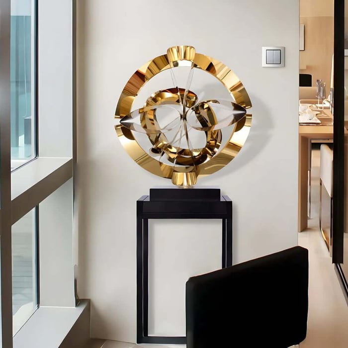 Gold abstract circular sculpture on a black pedestal in a modern interior.
