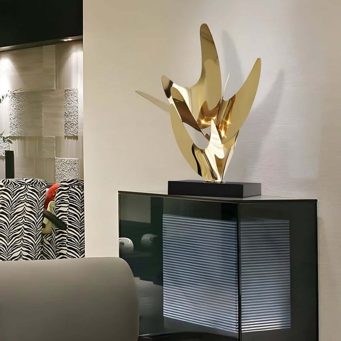 Shiny gold abstract sculpture on a black base atop a modern cabinet, styled in a contemporary living room.