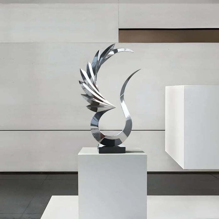 Reflective silver abstract sculpture with curved blade-like elements on a white pedestal against a minimalist wall.