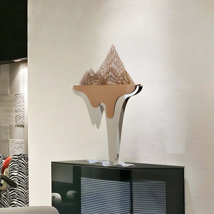Contemporary abstract sculpture with a white-and-gold form and wire-like crown, placed on a sleek black cabinet.