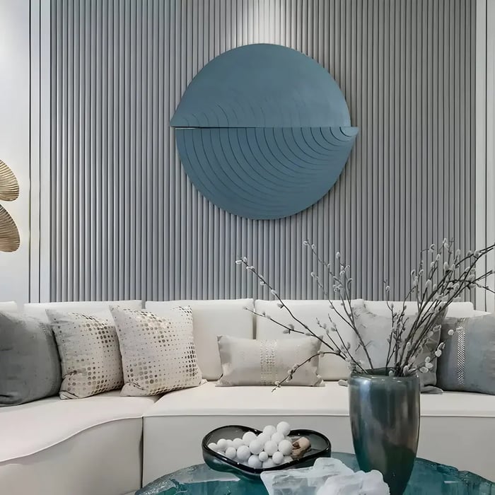 A large blue circular artwork with layered concentric ridges mounted on a slatted gray accent wall above a white curved sofa with decorative pillows.