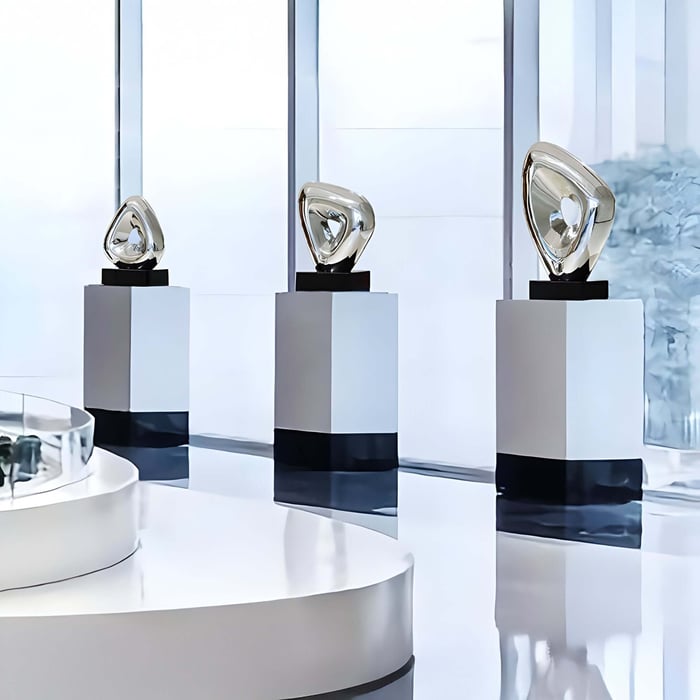 Three metallic abstract sculptures displayed on sleek square pedestals.