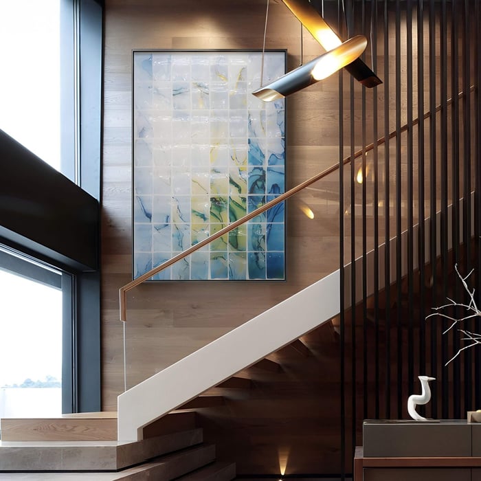 Abstract 3D acrylic wall art with blue, green, and yellow gradient tiles arranged in a grid, displayed on a wooden staircase wall with modern lighting.