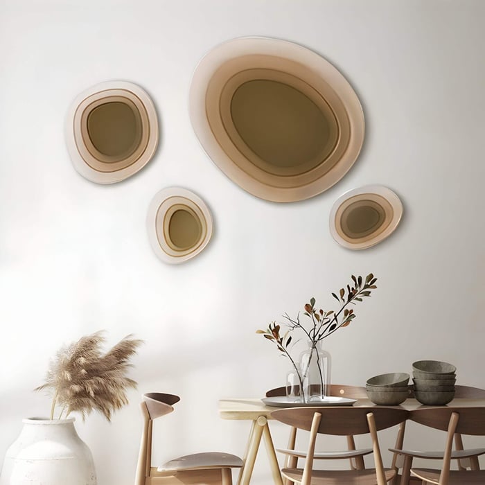 Four layered circular beige acrylic wall sculptures in varying sizes arranged above a dining table, creating a warm gradient cluster effect in a minimalist dining room setting.