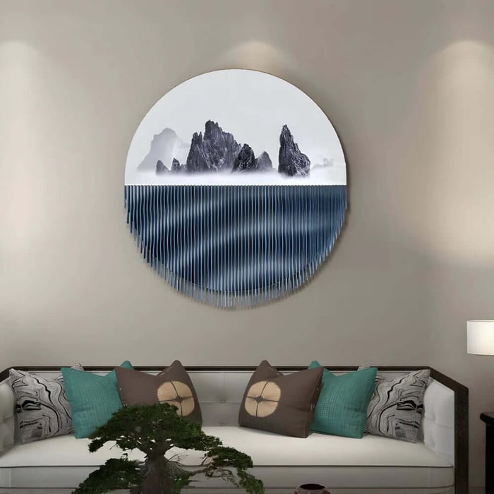 Circular wall art with misty mountains and blue fringe above a sofa with teal pillows.