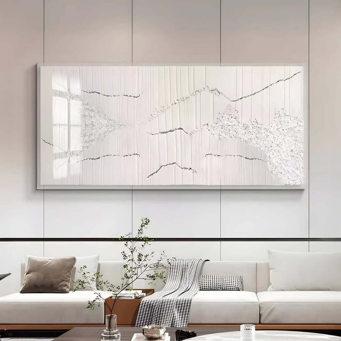 Minimal white textured abstract wall art with subtle cracks and raised areas above a light sofa in a clean, modern space.