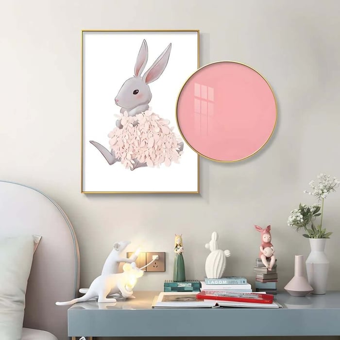 Cute rabbit illustration print on a bedroom wall beside a round pink wall mirror and bedside table decor.