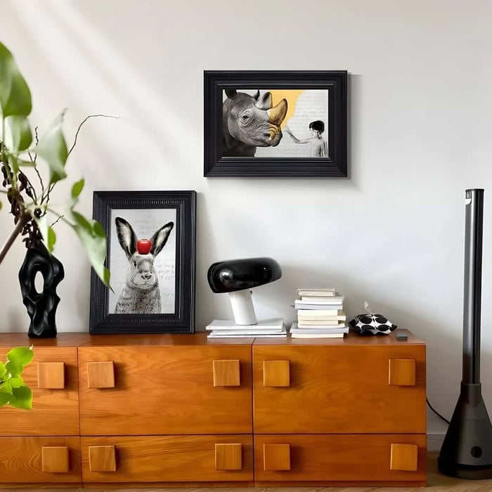 Two framed animal art prints on a wooden sideboard, including a rabbit portrait and a rhino artwork in a modern living space.