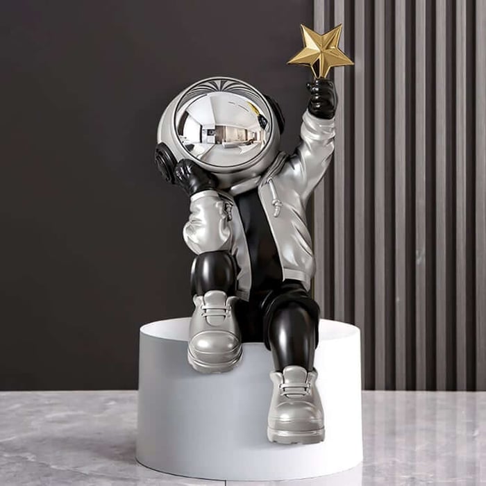 Silver astronaut figurine with a reflective helmet sits on a white pedestal, holding a gold star aloft in a modern gray interior with vertical wall slats.