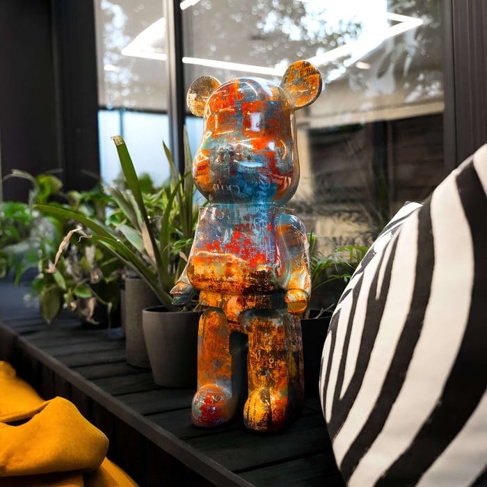 Vibrant obsidian bear sculpture with a distressed paint finish, displayed indoors among greenery and modern decor for artistic and contemporary styling.