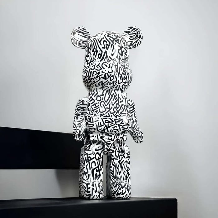 Black and white graffiti-style bear sculpture on a black bench in a modern minimalist room.