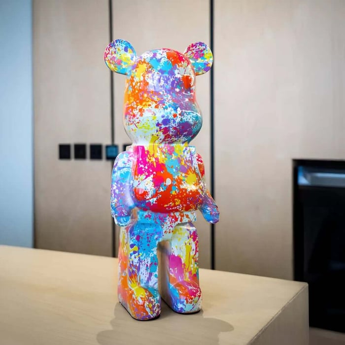 Colourful paint-splattered bear sculpture on a light wood counter in a modern interior.