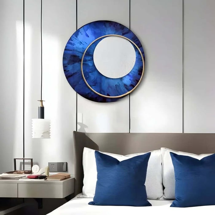 Modern bedroom with a grey headboard, white bedding and two blue cushions, featuring a large circular blue and gold wall artwork above the bed and a minimalist pendant light over a floating bedside table.