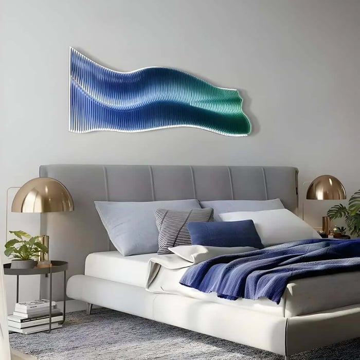 Modern bedroom with a grey upholstered bed, blue and white bedding, and a large wavy blue-to-green wall sculpture above the headboard, flanked by gold dome bedside lamps.