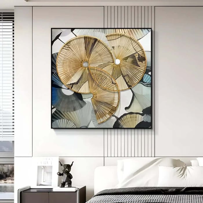 Modern bedroom with a white panelled wall featuring a large framed abstract artwork of overlapping gold fan-like circles above a bed with white bedding and a bedside table with a small black sculpture.