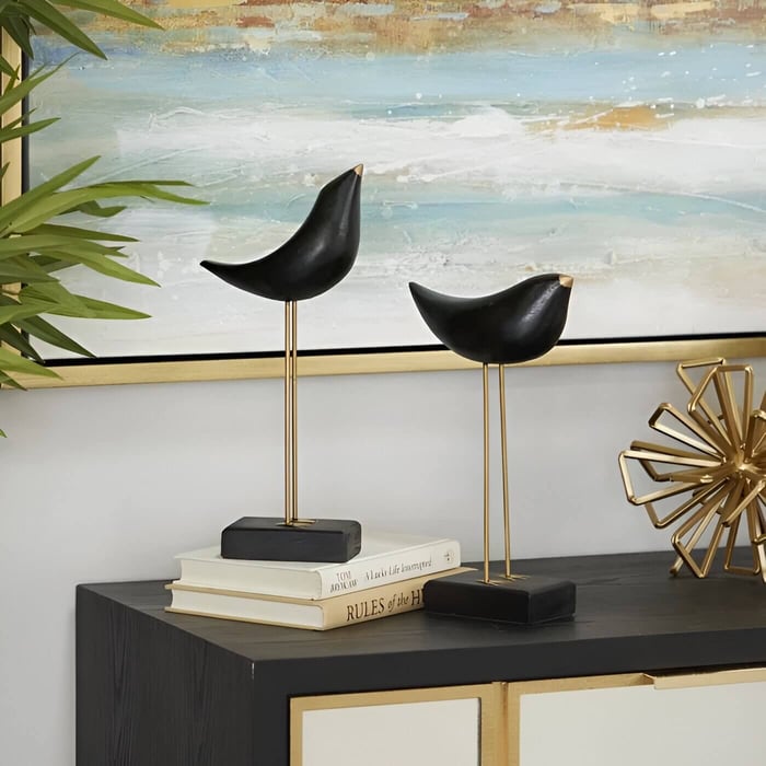 Elegant black bird sculptures with gold accents perched on a console table, styled with books, gold decor, and a serene abstract painting in the background.