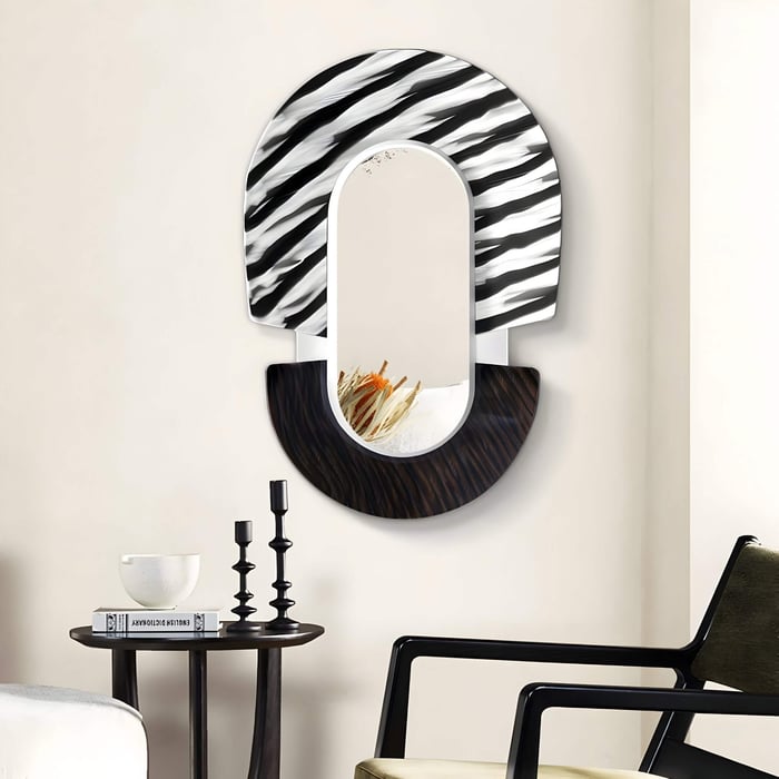 The Arcus Black & White Zebra Stripes Mirror 3D Wooden Wall Art by Giant Sculptures features a semicircular design with zebra stripes on top and a textured bottom. Below, a small shelf holds decorative dried grasses. Nearby, theres a table with candles and a bowl, plus a black chair in view.