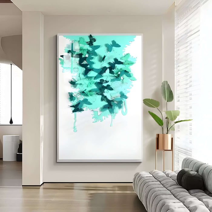 A modern office room highlights the Luminara Green II Butterfly Paper 3D Wall Art by Giant Sculptures in teal tones. A potted plant basks in sunlight beside a light gray sofa, with natural light filtering through tall, sheer curtains.