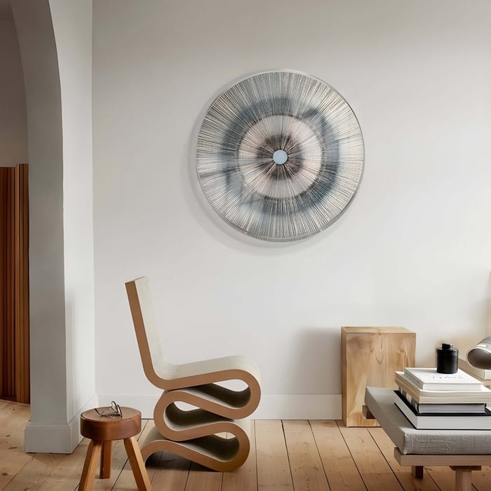 Round radial-patterned wall sculpture in neutral tones mounted above a sculptural chair in a cozy reading nook.