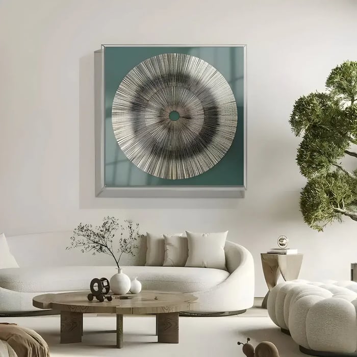 A modern circular wall art with a metallic silver finish, set against a teal background, displayed in a contemporary living room with a minimalist sofa and décor.