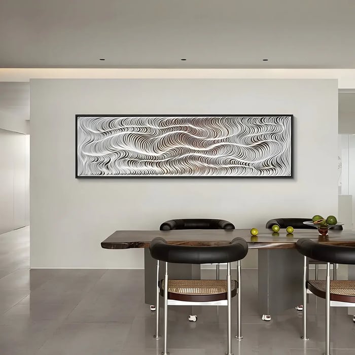 A large horizontal black-and-white abstract art work with a fluid wavy pattern displayed above a wooden dining table with black chairs and fresh green apples.