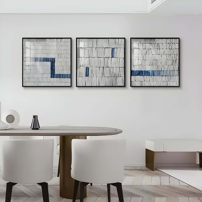 Minimalist Triptych Artwork with Textured Layers – A set of three framed abstract panels featuring layered white textures with sporadic blue accents, creating a modern yet organic effect in a contemporary dining space.