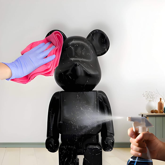 Close-up of cleaning a black bear sculpture with a glossy effect using a spray bottle and cloth, demonstrating proper care for luxury resin statues.