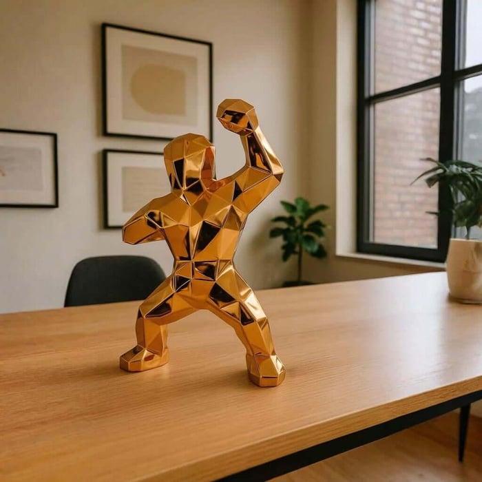 Gold geometric gorilla sculpture flexing its arm on a modern wooden office desk.
