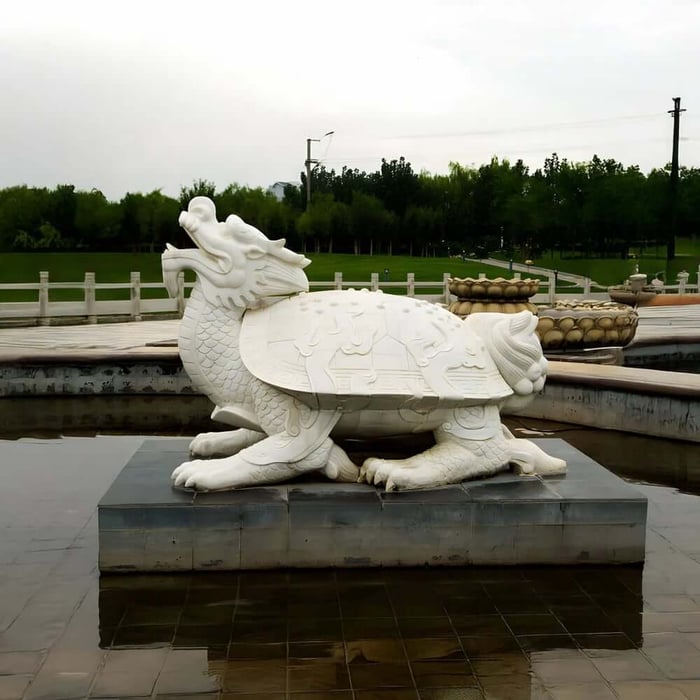 White stone dragon-turtle statue beside a reflecting pool in a landscaped park.