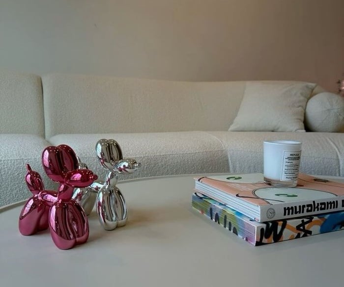 Modern coffee table styled with metallic pink and silver balloon dog sculptures, stacked art books, and a minimalist candle, set against a cream textured sofa in a cosy living space.