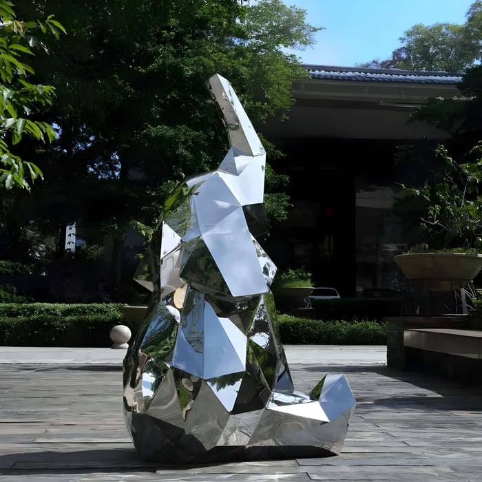 Outdoor geometric mirrored elephant sculpture reflecting its lush green surroundings, displayed in a modern courtyard setting under a clear blue sky.