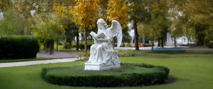 White angel sculpture reading a book in a garden