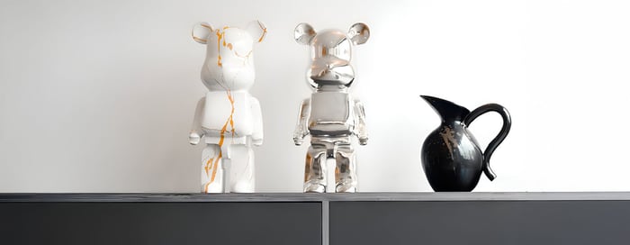 Stylish display featuring white and chrome bear sculptures with gold detailing, accompanied by a sleek black ceramic vase, placed on a modern grey cabinet against a white wall.