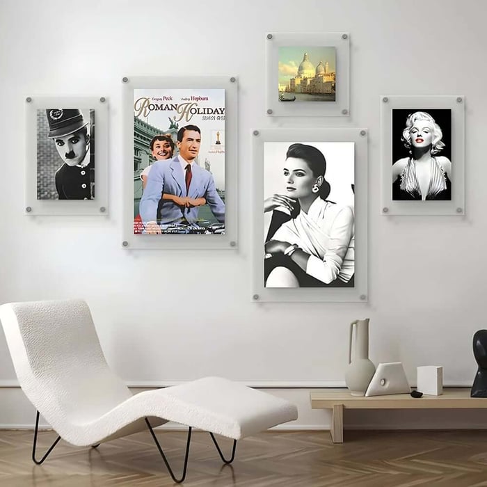 Minimalist room with a white lounge chair and a gallery wall of framed vintage film posters, portraits, and a small landscape print.