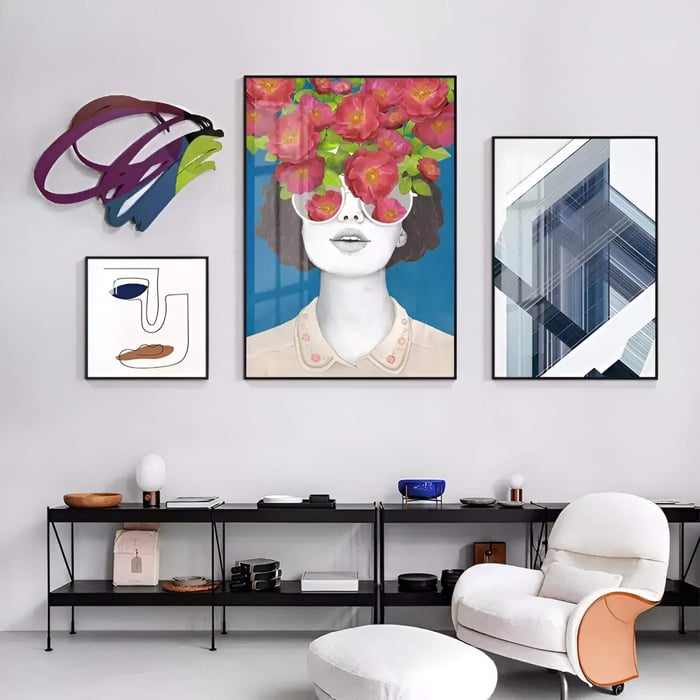 A modern living space featuring the Cavoya Multiform Expression 4-Set Wall Art, including a colourful abstract metal piece, a floral portrait, a geometric print, and a minimalist line artwork, creating a lively gallery wall above a black console and white armchair.