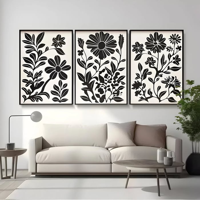 Black floral triptych wall art above a modern cream sofa in a minimalist living room.
