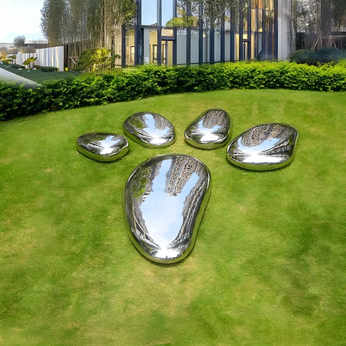 A unique outdoor art installation featuring oversized reflective stainless steel pieces arranged in the shape of an animal paw print on a manicured lawn.