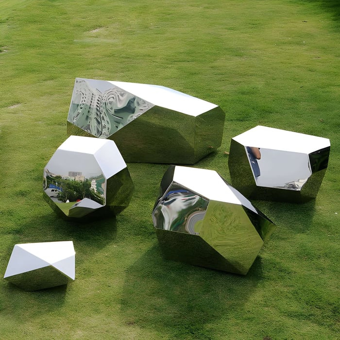 Cluster of geometric mirrored sculptures arranged on a lush green lawn, reflecting the natural surroundings and open sky.