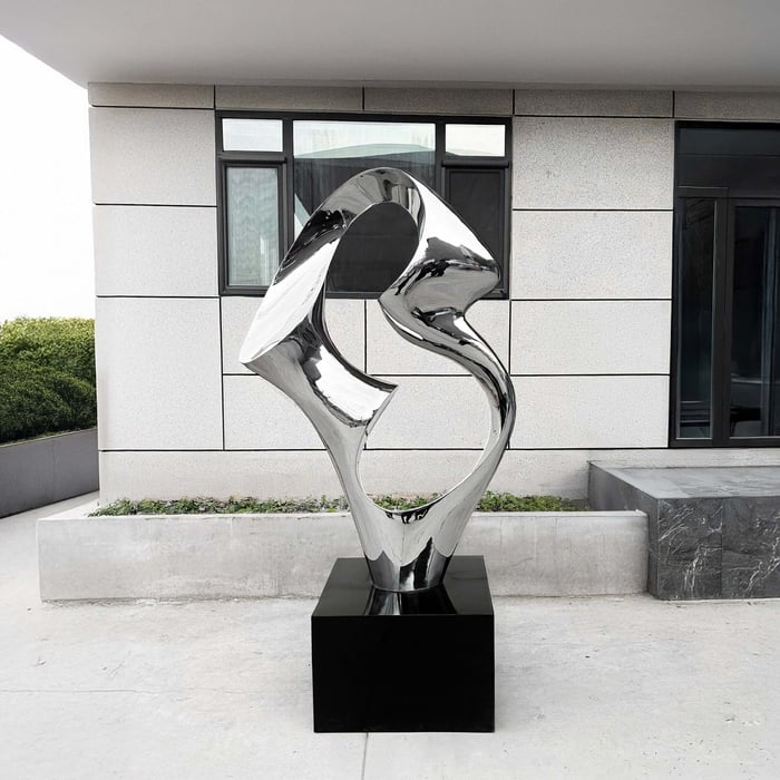 Abstract silver metallic sculpture displayed outside a modern building.