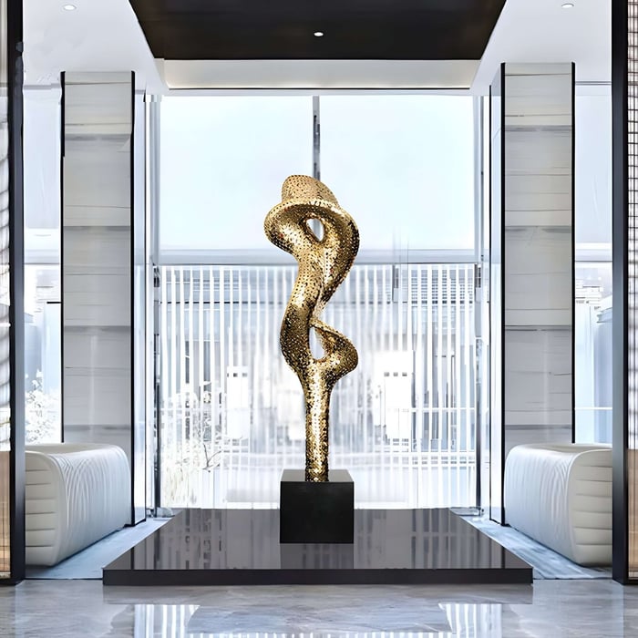 Tall twisting golden sculpture with perforated texture in a bright interior.
